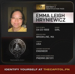 grey ID  card, On the left a photo of a smiling brunette with glasses wearing a yellow shirt over a seal with a factory with cogs in the middle and a circle outside that says district at the top and 3 at the bottom accentuated with two sheafs of wheat, and technology underneath. On the right, a golden capitol flag with the a eagle with the words next to it saying Government of Panem, underneath that District 3 Identification Pass. Under that on a silver stripe: Emma Leigh Hryniewicz and below that Date of Birth: 04-22-1988, Gender: Girl, Migrated from Brookline, MA Country USA, Assigned Occupation: Engineer, Panem Citizen Number (PCN): PNDMN1.BK1311 and underneath in red Identify yourself at thecapitol.pn